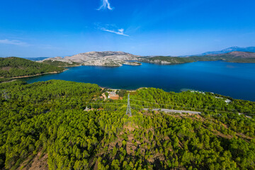 Aerial view of Komani Lake in Albania, showing deep blue water surrounded by green forested hills and rocky mountains under a clear sky, highlighting the lake s remote and scenic natural beauty.