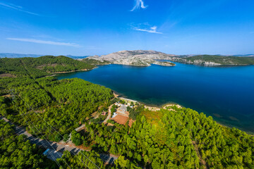 Aerial view of Komani Lake in Albania, showing deep blue water surrounded by green forested hills and rocky mountains under a clear sky, highlighting the lake s remote and scenic natural beauty.