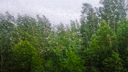 Obraz premium Landscape view through the glass of a train covered with raindrops while driving.
