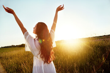 Fototapeta premium Vacation, back and woman at field for freedom on adventure, travel or summer holiday in countryside. Arms up, meadow and person in nature on getaway trip at sunset with flare, space and peace outdoor