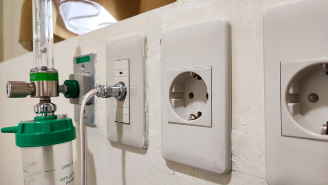 close-up shot of essential hospital wall equipment, including an oxygen flowmeter with humidifier bottle, medical gas or data port, and European-style power sockets (Type F)