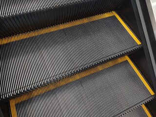 High-angle detailed view of mechanical escalator steps, highlighting metallic ridges and bright yellow safety edges. Urban movement, public infrastructure, and modern architecture concept background