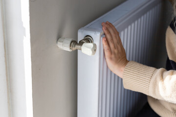 Close-up of a hand adjusting the temperature on a radiator thermostat, regulating home heating for energy efficiency