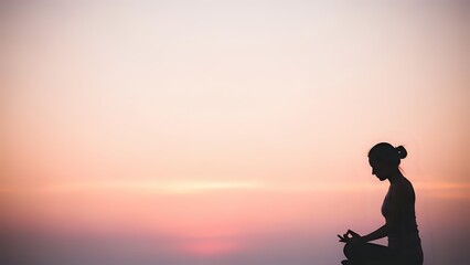 Obraz premium Young woman meditating in lotus pose during sunset with peaceful pink sky background for wellness and mindfulness practices.