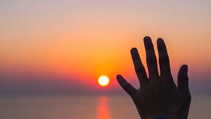 Silhouette of human hand reaching toward golden sunset over calm water creating peaceful moment of connection with nature and tranquil evening atmosphere.