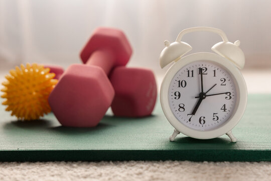 Alarm clock, yoga mat and dumbbells close-up. Morning physical jerks, fitness concept