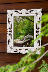 A white carved mirror on a wooden wall reflecting the beauty of a summer garden