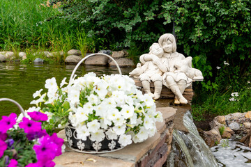 Decorative metal planter basket with blooming white petunias next to the pond in the summer garden