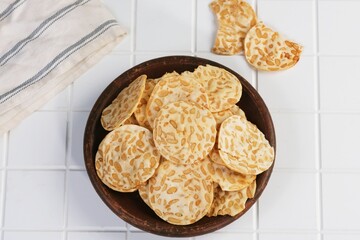 Top view of crispy tempe chips or keripik tempe in wooden bowl on white surface.
