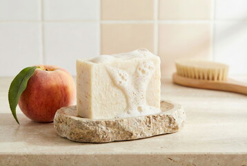 Natural bar soap with rich lather on a stone dish, alongside a fresh peach and bath brush, evoking a clean, gentle, and refreshing self-care routine.