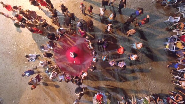 Romani people dance in circle at outdoor village wedding henna night celebration. Overhead view shows bride red dress guests clapping during ethnic halay party.