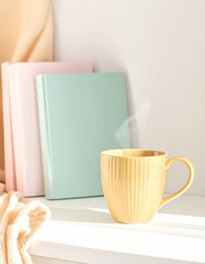 Yellow textured mug with steaming coffee and books
