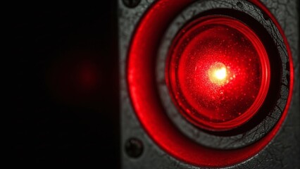 Extreme close-up of a glowing red industrial indicator light mounted on a dark textured surface