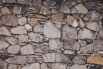 Obraz premium A wall constructed using different sizes and shapes of gray and brown stones arranged closely. The stones show natural textures and colors that create a structured surface full of character