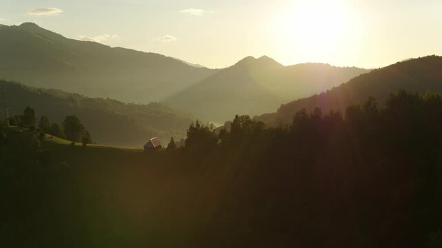 Cinematic golden hour drone shot of misty mountains and a lonely house in the Transylvanian countryside.
