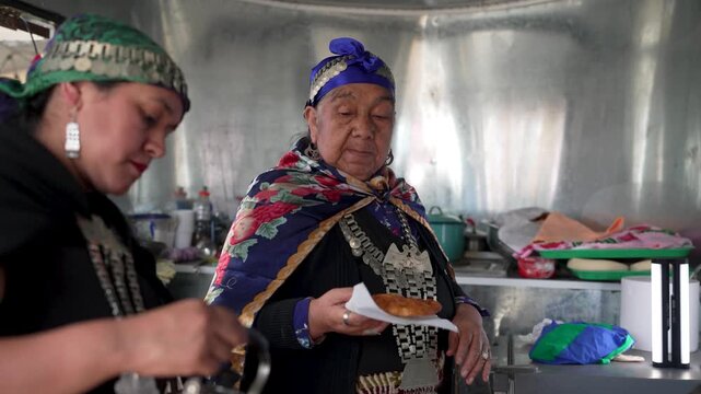 Indigenous mapuche women in traditional clothing sharing a meal and drinking mate from a bombilla