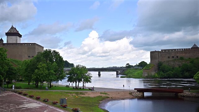 View of the Narva River bridge border between Estonia and Russia, showing Narva Castle, Ivangorod Fortress on a cloudy daytime summer scene.