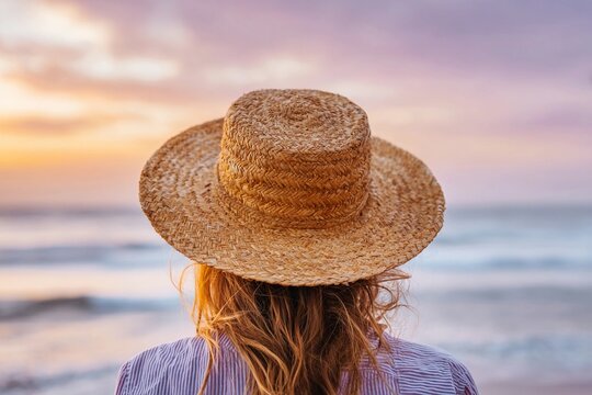 Looking at the ocean horizon with a straw hat during sunset in soft pastel sky - Powered by Adobe