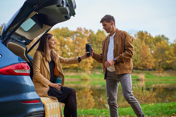 Man and woman with thermos cups near car by lake