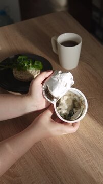 Vertical video opening aluminum lid on yogurt cup with spoiled dairy product affected by harmful mold. Everyday nutrition routine turns dangerous, risk of allergy from mold exposure