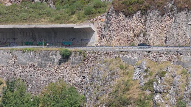 Car driving on a mountain road under a rockfall protection wall in Spain.