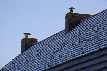 Red brick chimneys on a frosty roof with snow-covered tiles under a clear blue sky