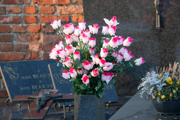 Pink and white artificial roses in a stone vase on a grave with a brick wall background