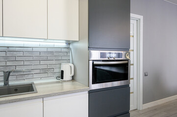 Fototapeta premium modern kitchen with white upper cabinets, dark grey lower units, a stainless steel oven, grey brick-style backsplash, light wood countertop, and a white electric kettle