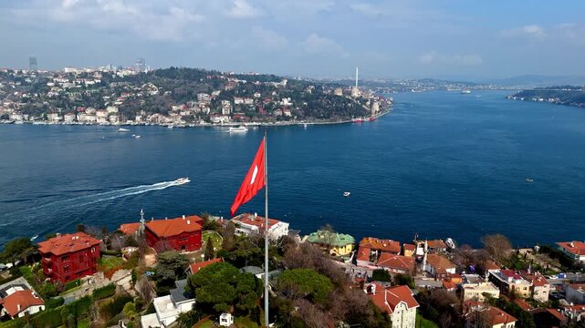 Aerial drone footage showing the large Turkish flag in Kandilli overlooking the Bosphorus, with red-roof homes, waterfront residences and the deep blue strait creating a striking coastal landscape.