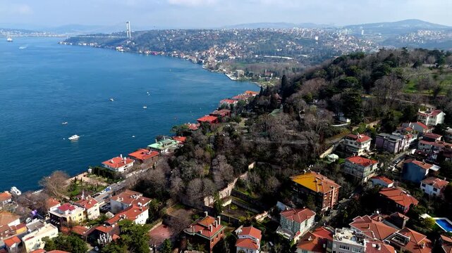 Aerial drone footage of the Kandilli and Vanikoy coastline along the Bosphorus in Istanbul, showing hillside residences, red-roof homes, coastal roads and the wide blue strait stretching into the dist