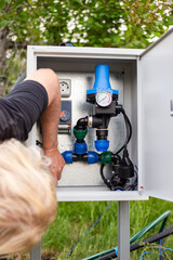 A technician performs maintenance and adjustments to the internal components of a garden irrigation system control panel