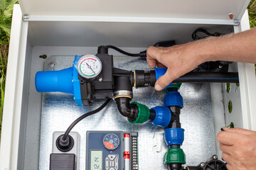 A close-up of a worker's hands adjusting a blue plastic fitting inside an irrigation system control unit. Installing the irrigation system's automation