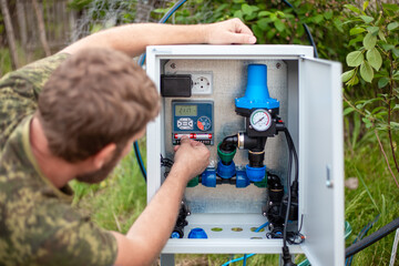 A man installs a digital automatic irrigation controller and checks the batteries in the outdoor unit