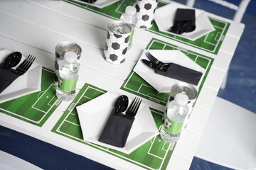 Top view of a soccer-themed party table featuring football field placemats, black cutlery, white...