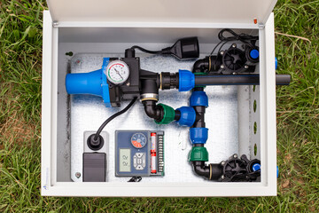 A top view of a white metal irrigation system control unit containing a water pump, pipes, pressure gauge, and digital timer
