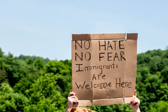 A protestor at a political rally holds a sign that reads "no hate, no fear, immigrants are welcome here," advocating for immigrant rights, acceptance and community inclusion.