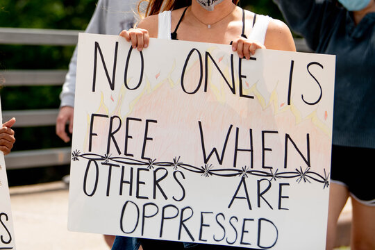 Activist holds white cardboard sign reading "No One is Free When Others Are Oppressed" during peaceful political demonstration. Message emphasizes interconnected nature of freedom and social justice