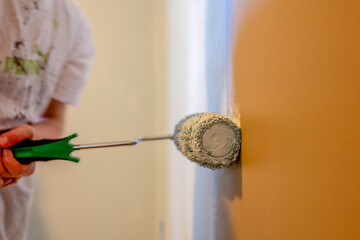 Rolling a fresh coat of paint on a wall using a paint roller in a bright room with soft lighting