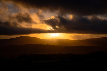 Cloudy dark sunset, silhouetting mountains, woods and hills; featuring Moel Famau. Clwydian Hills, Clwyd, Wales