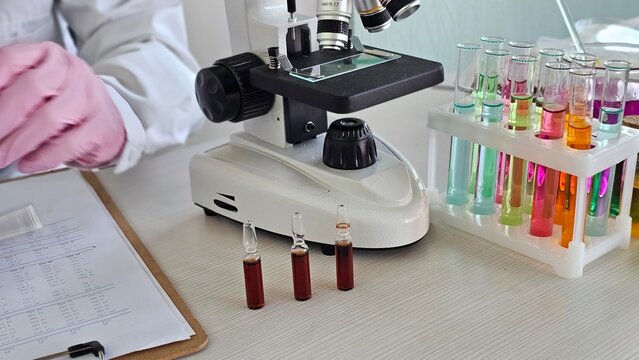 Scientist working at lab with microscope and test tubes during research process - Powered by Adobe
