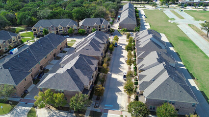Townhomes align along a central drive near dense tree buffers west of Gerault Road. Brick textures and dark shingle roofs contrast with soft shadows and parked vehicles, Flower Mound, Texas