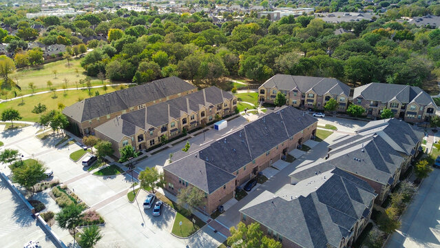 Multi-unit homes and white moving container near curved drive and tree canopy off Old Settlers Road. Brick walls, asphalt roofs reflect winter light across landscaped medians, Flower Mound, Texas