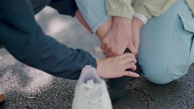 female jogger suffering from a sprained ankle receiving help from her friend. They are treating a muscle cramp and leg pain after an intense running session on the city street sidewalk.