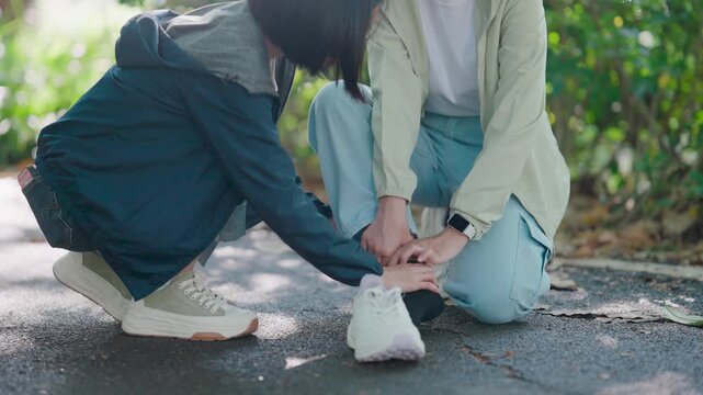 Sporty woman massaging the twisted ankle of her friend after a fitness accident. They sit on the ground in a park treating a painful leg injury caused by running and exhaustion during a workout.