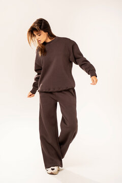 Beautiful, natural woman with long hair posing in studio, wearing comfortable brown tracksuit with an oversized sweatshirt and sporty shoes. Full length photo. 