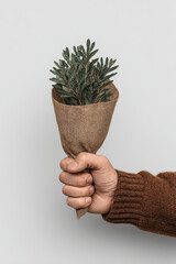 Hand holding a small bouquet of green leaves wrapped in burlap
