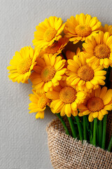 Vibrant bouquet of yellow daisies wrapped in burlap against a textured gray background