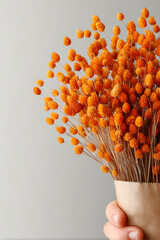 Hand holding a bouquet of dried orange bunny tail grass in a brown paper bag
