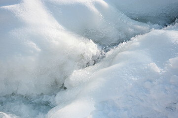 Close-up of icy river surface with frozen textures, cracks and flowing cold water, abstract winter nature background.