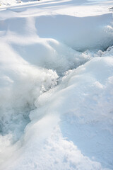Close-up of icy river surface with frozen textures, cracks and flowing cold water, abstract winter nature background.